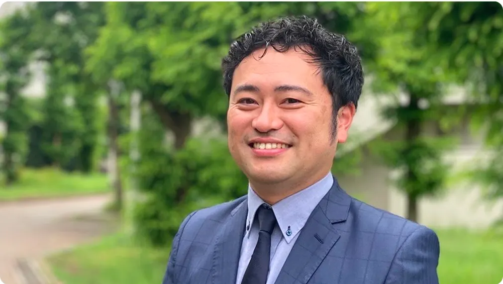 나무가 우거진 길을 배경으로 정장 차림으로 웃고 있는 기숙사장
