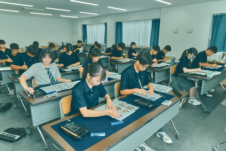 교실 책상에 붓과 화선지를 펴고 신년 서예를 하는 학생들