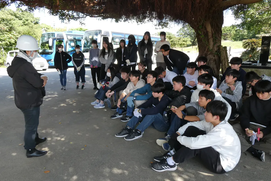 오키나와 연수 여행 중 큰 나무 그늘에 앉아 현지 안내인의 설명을 듣는 학생들