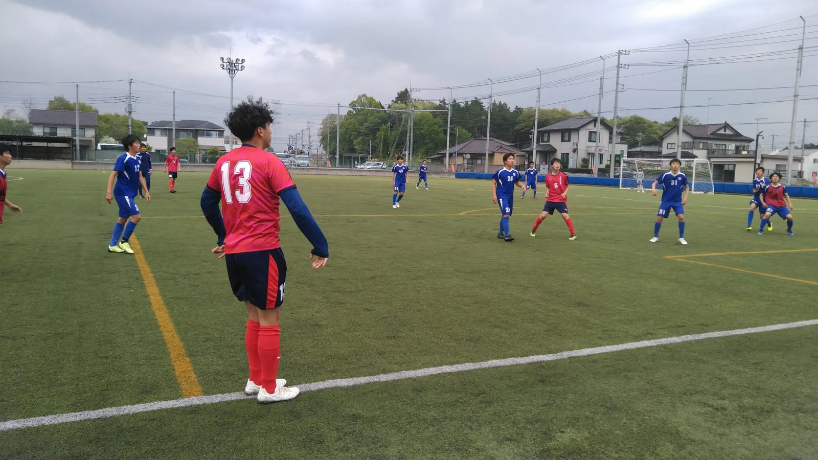 인조 잔디 운동장에서 빨간 유니폼의 축구부 선수들이 파란 유니폼 팀과 경기하는 모습