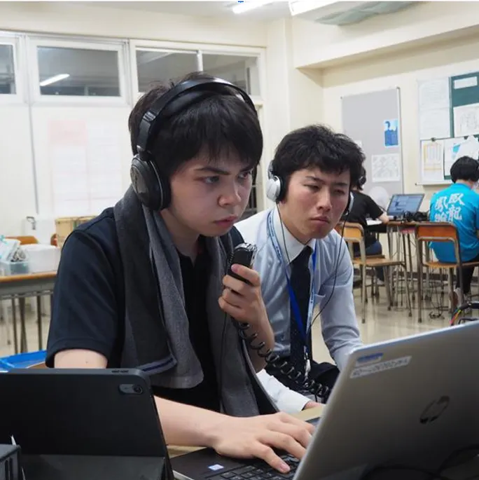 교실에서 헤드폰을 쓰고 무선기 마이크를 든 채 노트북을 보며 교신하는 학생과 옆에서 함께 듣는 선생님