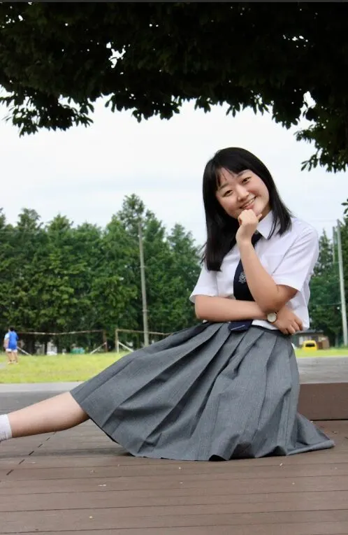 나무 그늘 아래 데크에 앉아 턱에 손을 대고 웃는 교복 차림의 I 학생