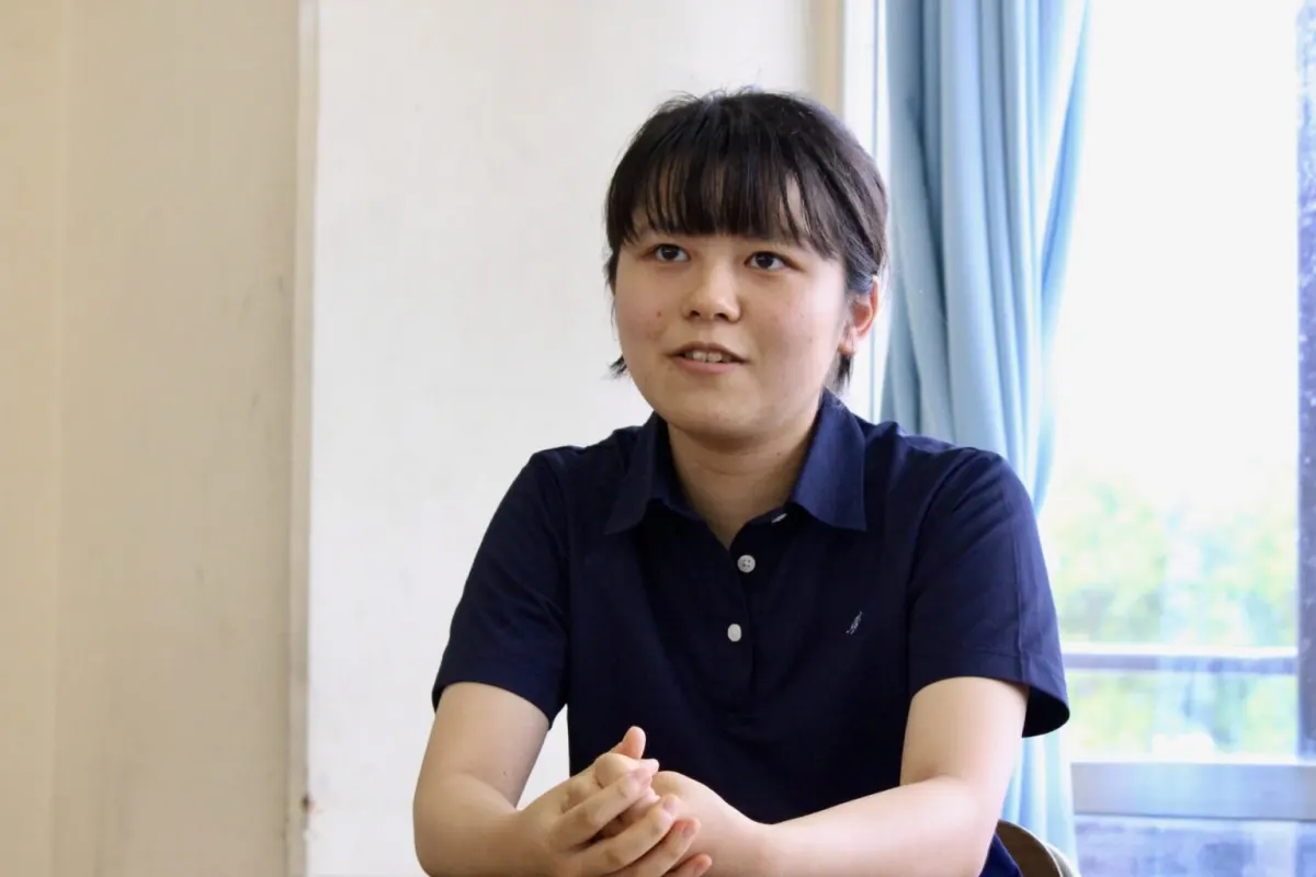 창가 교실 책상에서 두 손을 모으고 이야기하는 남색 폴로셔츠 차림의 C 학생