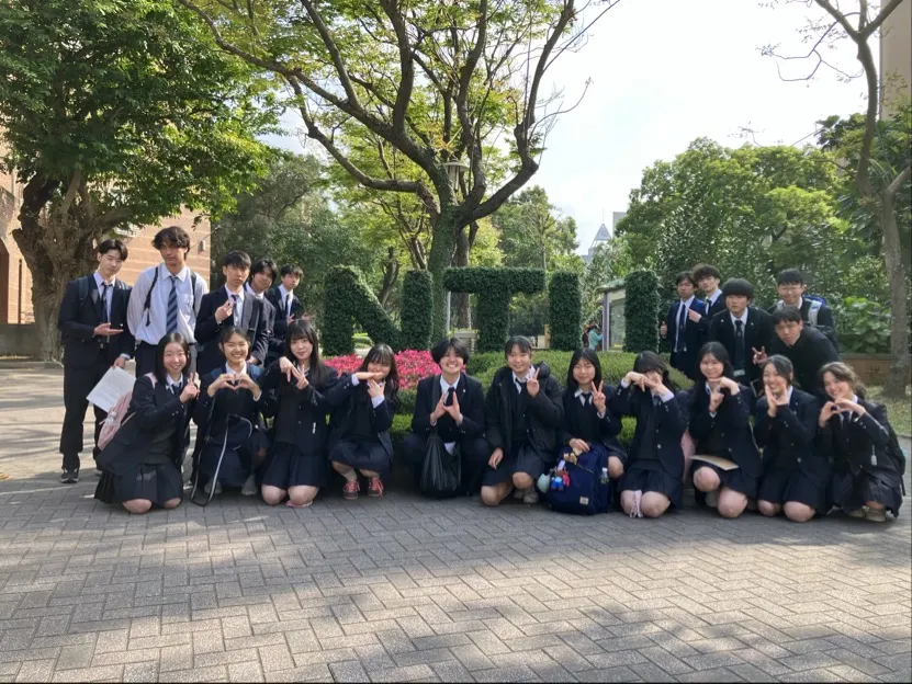 나무가 우거진 광장에서 하트와 브이 포즈로 단체 사진을 찍은 교복 차림 참가 학생들