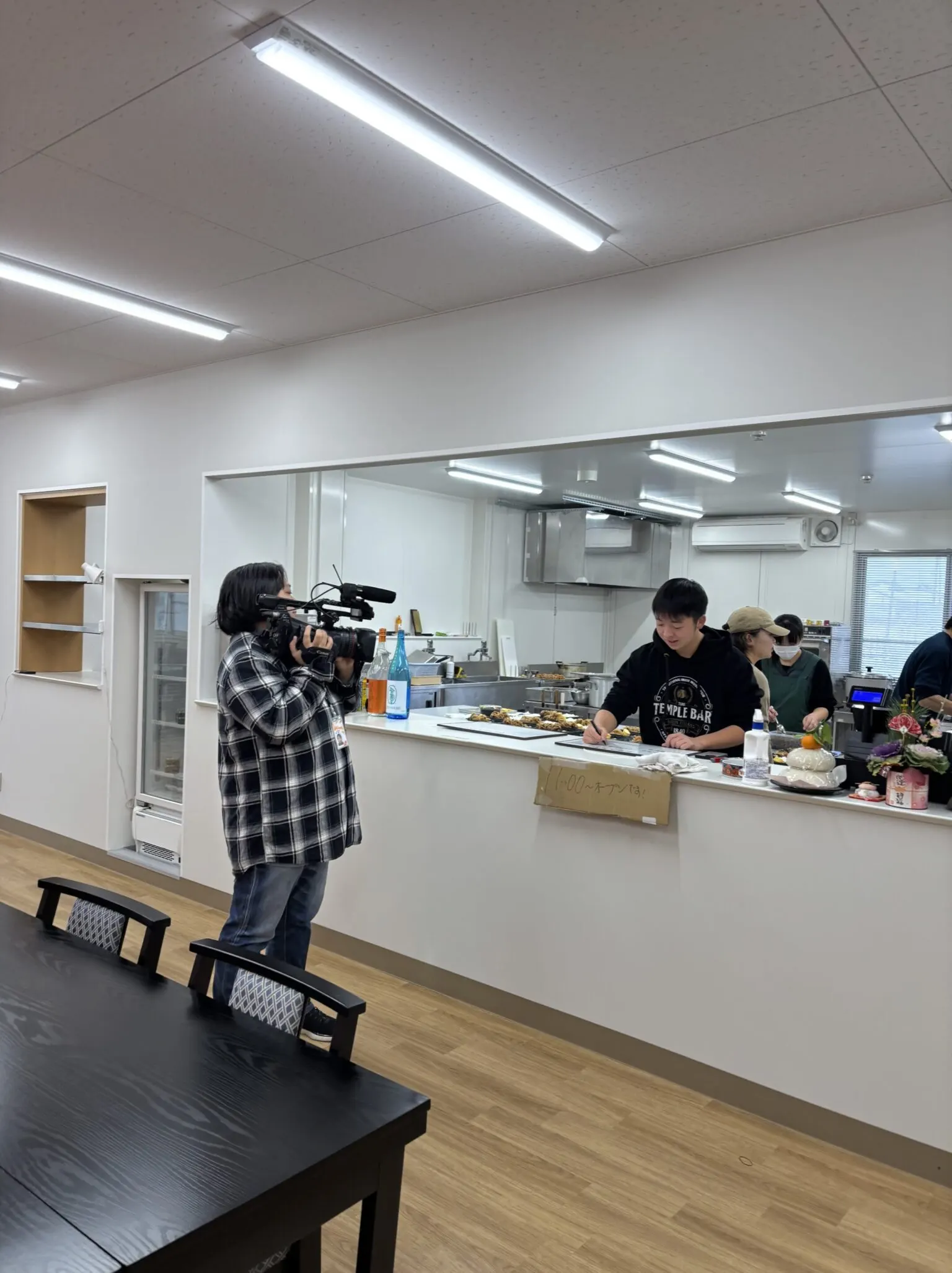 새로 지은 식당 주방 카운터에서 학생이 글씨를 쓰고 그 모습을 방송 카메라가 촬영하는 장면