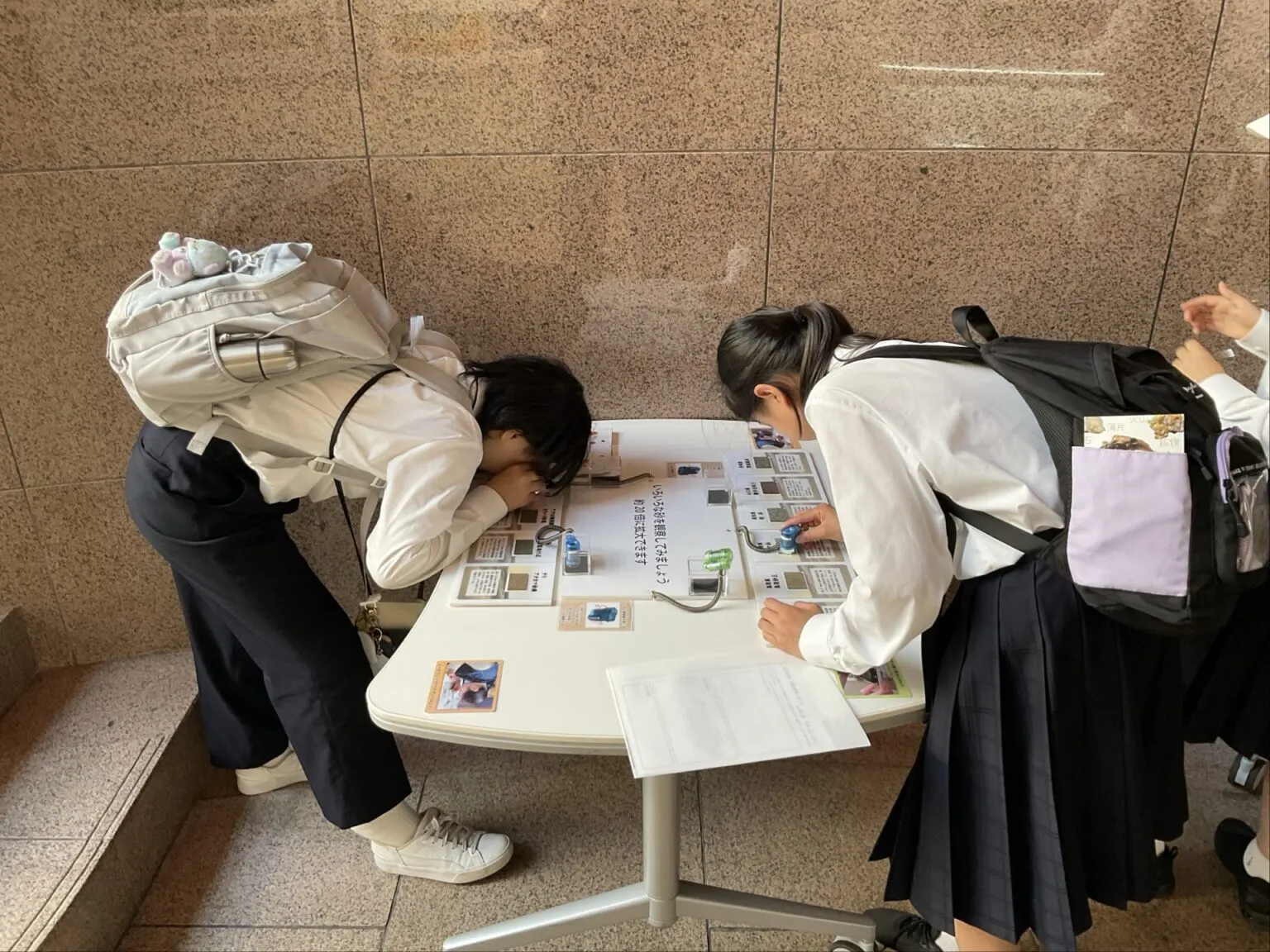 여러 가지 모래를 약 20배로 확대해 보는 전시 탁자에 몸을 숙여 관찰하는 학생 두 명