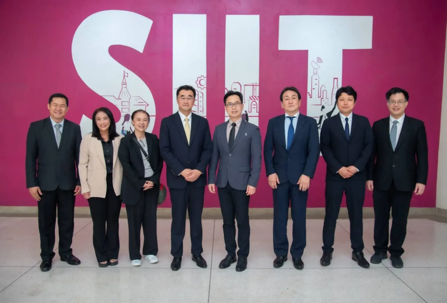 분홍색 벽에 크게 그려진 SIIT 글자 앞에 정장 차림의 양교 관계자 8명이 서서 찍은 단체 사진