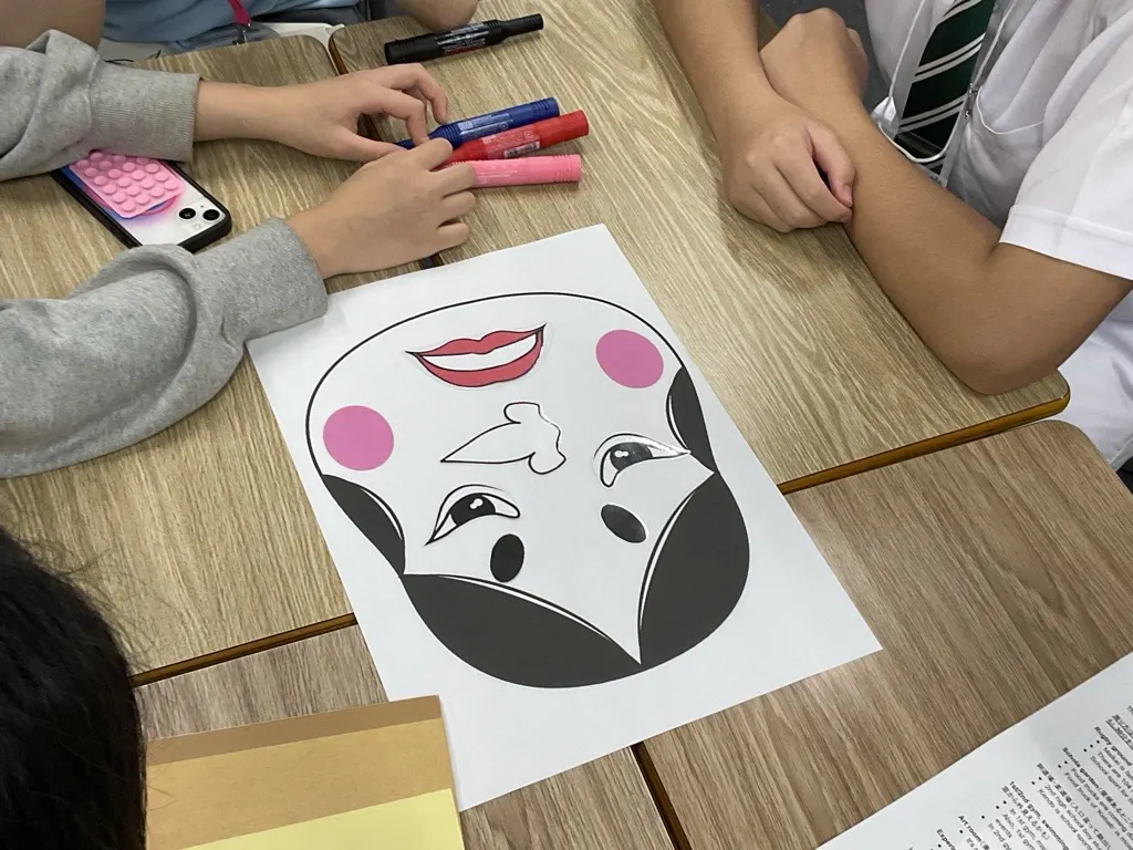 책상 위에서 눈, 코, 입 조각을 얼굴 그림에 붙여 완성한 후쿠와라이