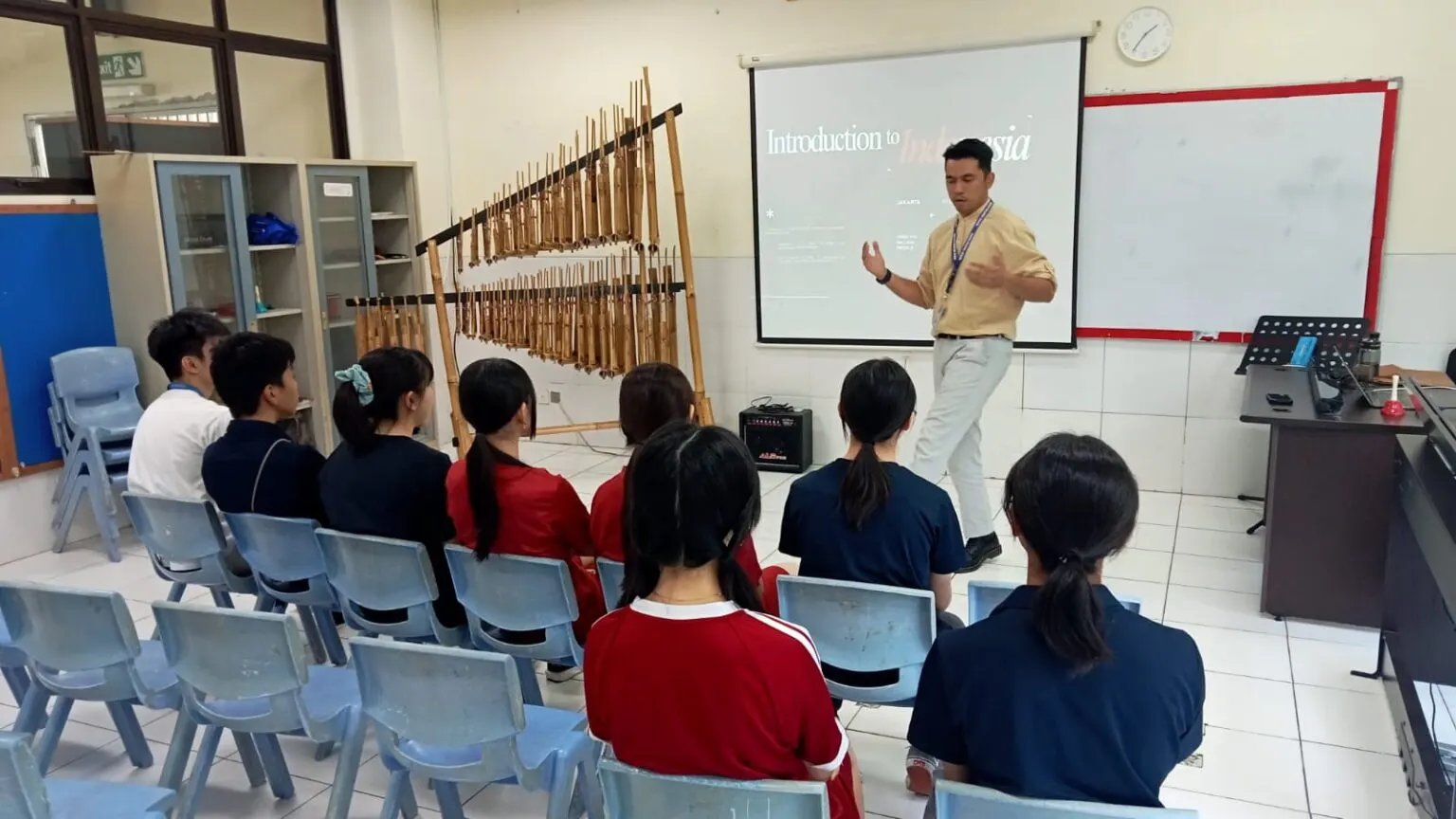 대나무 악기 앙클룽이 놓인 교실에서 Introduction to Indonesia 화면을 띄우고 설명하는 현지 교사와 듣는 학생들