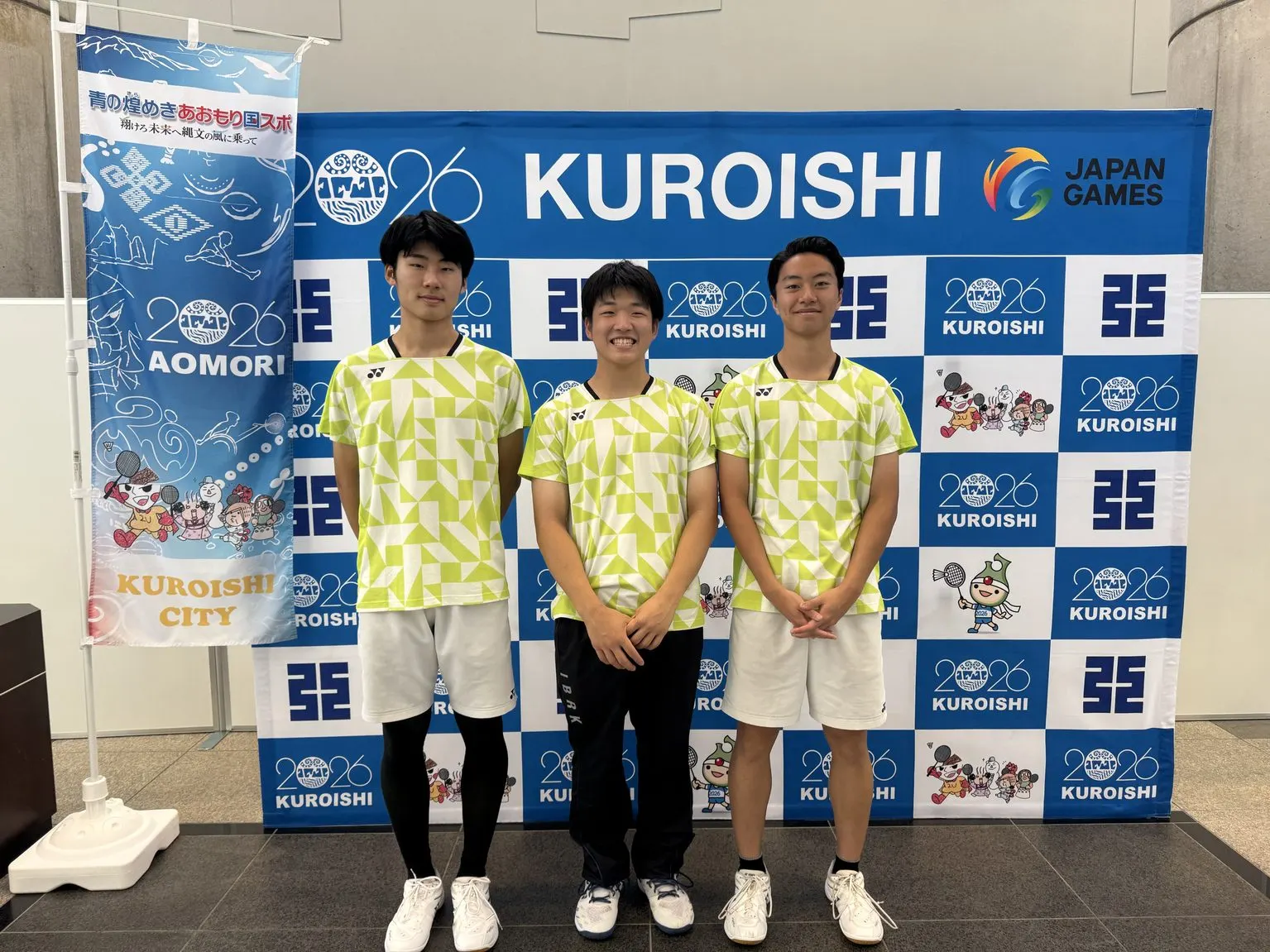 2026 KUROISHI 국민스포츠대회 배경판 앞에 연두색 유니폼을 입고 선 남자 선수 세 명