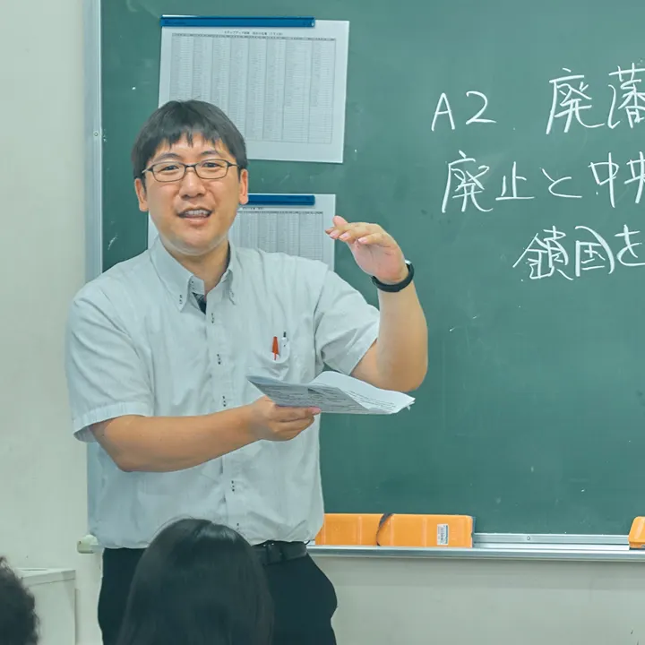 칠판 앞에서 자료를 들고 설명하는 사회과 교원